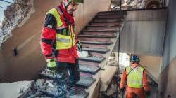 two men in safety gear examine the ruins of a building 