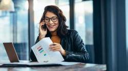 Woman sitting at table with laptop reviewing finances as she talks on her cellphone