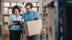 Female Inventory Manager Shows Digital Tablet Information to a Worker Holding Cardboard Box