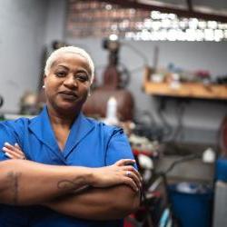 black woman wearing blue shirt in mechanics shop with arms folded 