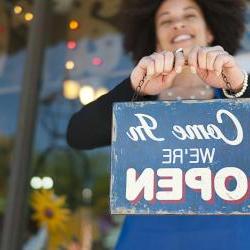 Woman holding vintage open sign up outside of a boutique store front.