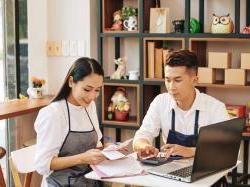 Young cafe owners sitting at table, checking bills and paying online